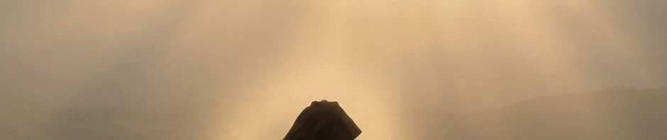 A cloaked figure meditating on a rocky cliff as sunbeams pierce through cloudy skies.