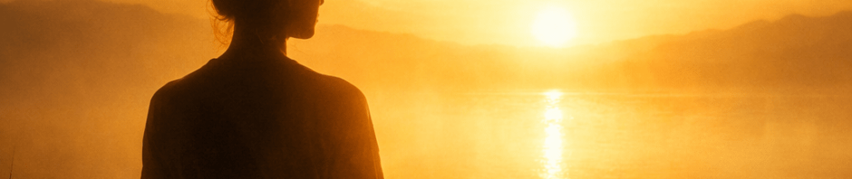 Silhouette of person sitting cross-legged meditating at sunrise by lake