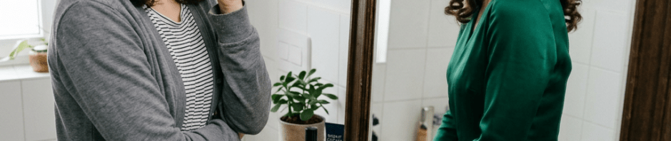 Woman looking worried while her mirror reflection shows her confidently smiling wearing a green dress
