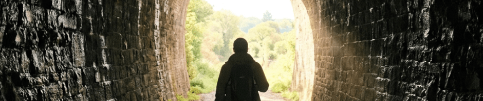 Person walking inside a stone tunnel toward the bright light at the exit
