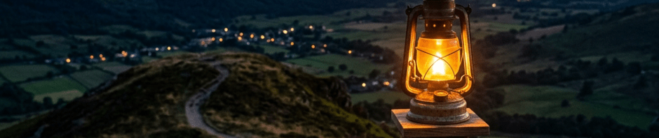 Lit lantern on wooden post on mountain trail with valley and sunset in background