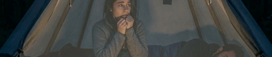 Woman sitting inside tent shivering with man sleeping beside her